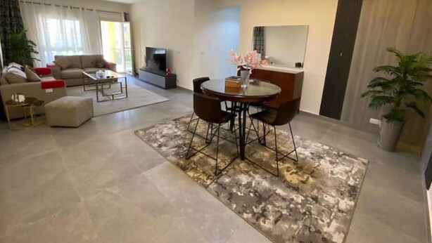 A modern living room with a sofa, coffee table, and a dining area with chairs. There is a TV and a plant in the room. - Elegant 2 bedrooms 2B swimming pool in Dream Land (Giza Governorate)