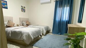 A bedroom with two beds, a blue curtain, a potted plant, and a small rug. - Elegant 2 bedrooms 2B swimming pool in Dream Land (Giza Governorate)