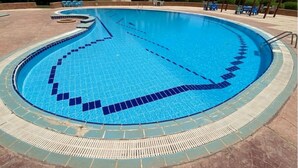 Une grande piscine circulaire, bordée de carreaux et entourée d’une zone aménagée pour se détendre.