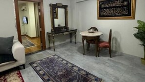 A living room with a sofa, a coffee table, a dining table with chairs, a rug, a mirror, and a wall-mounted decoration.