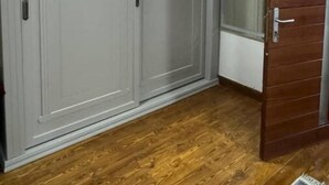 A room with a grey wardrobe, a wooden door, and a wooden floor.