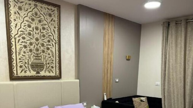 A hotel room with a bed, a nightstand, a black chair, and a decorative wall piece.