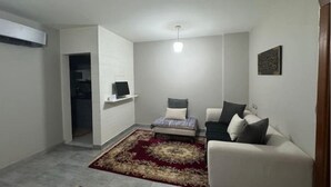 A living room with a sofa, a small bed, a TV on a shelf, and a patterned rug.