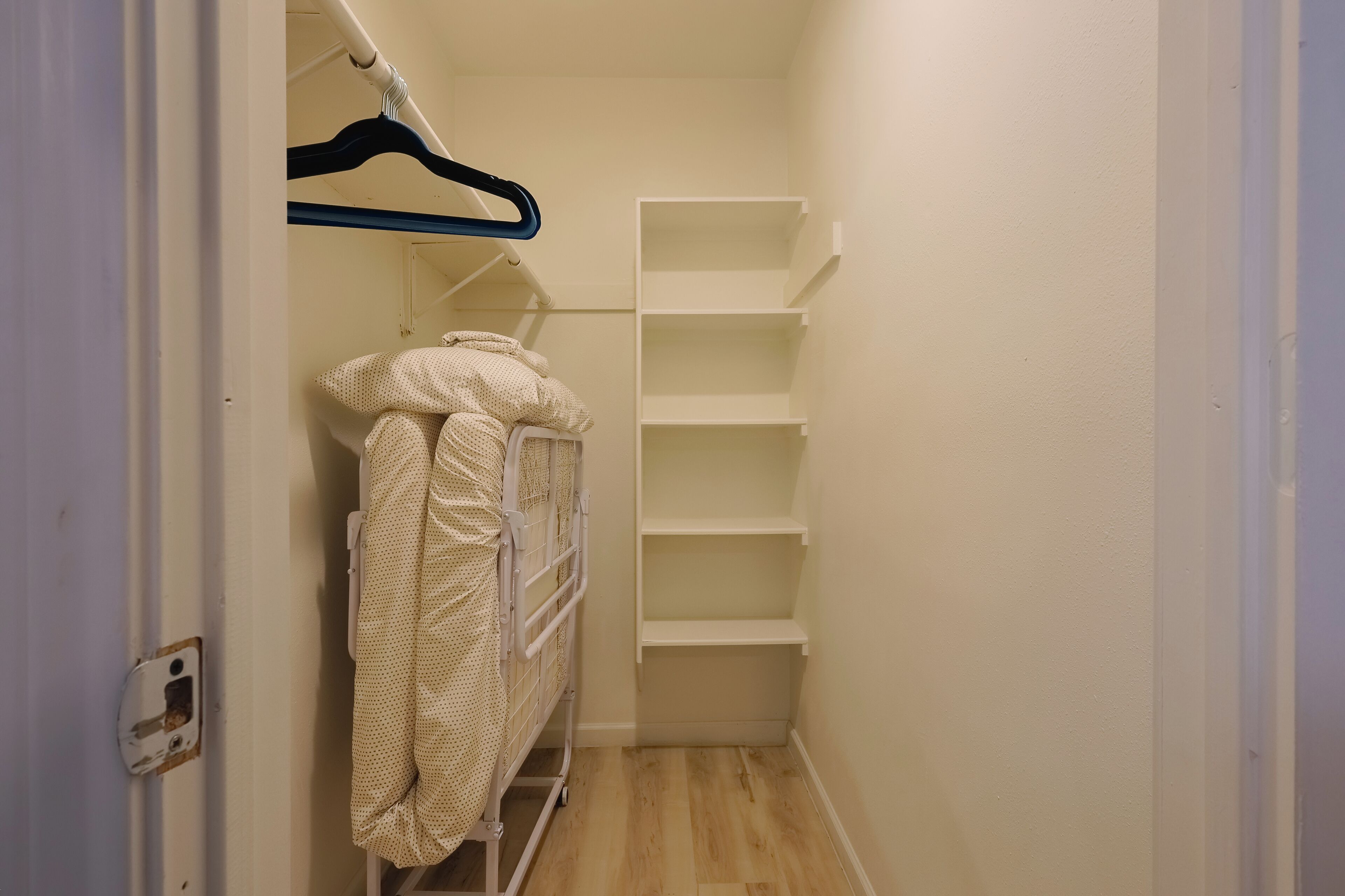 A narrow hallway with a white metal bunk bed and a white shelving unit.