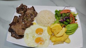 Une assiette composée de viande grillée, d’œufs au plat, de riz, d’une salade et de chips de bananes plantains.