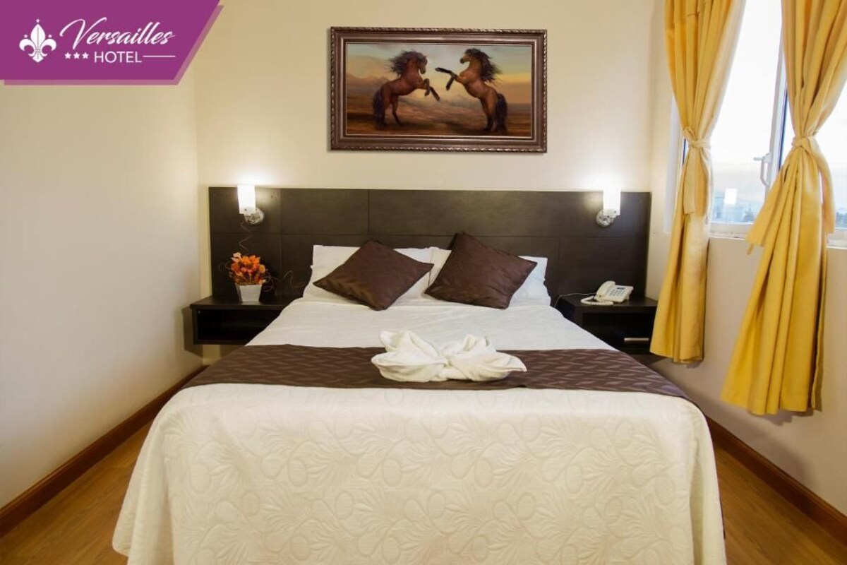 A hotel room with a large bed, two nightstands, a painting of horses, and a window with curtains.