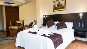 Une chambre d’hôtel avec un grand lit, une chaise en bois, une petite table avec un vase et un tableau accroché au mur.