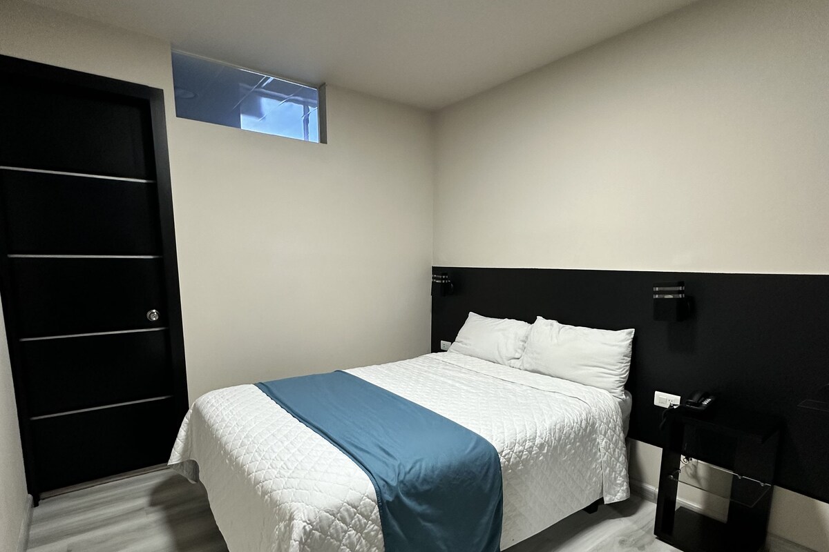 A bedroom with a bed, a nightstand, a black wardrobe, and a small window.