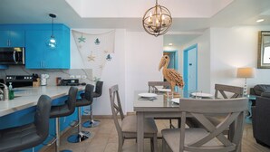 A modern kitchen with blue cabinets, a dining area with a wooden pelican decoration, and a chandelier.