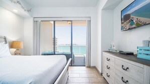 A hotel room with a bed, a nightstand, a dresser, and a view of the ocean through a sliding door.