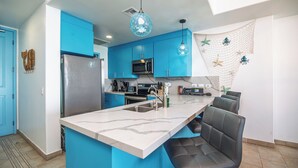 A modern kitchen with blue cabinets, a marble island, and a seating area with chairs.