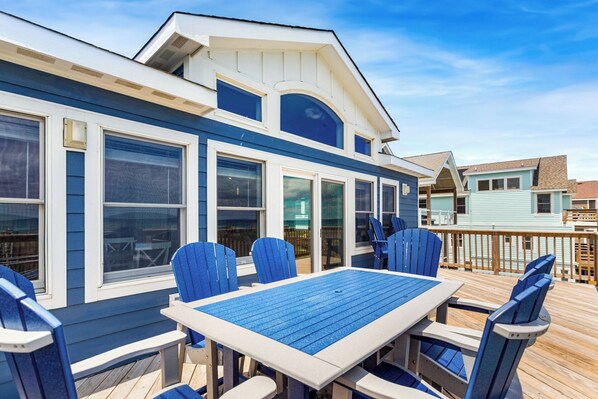 A deck with a table and chairs, overlooking a beach area with houses.