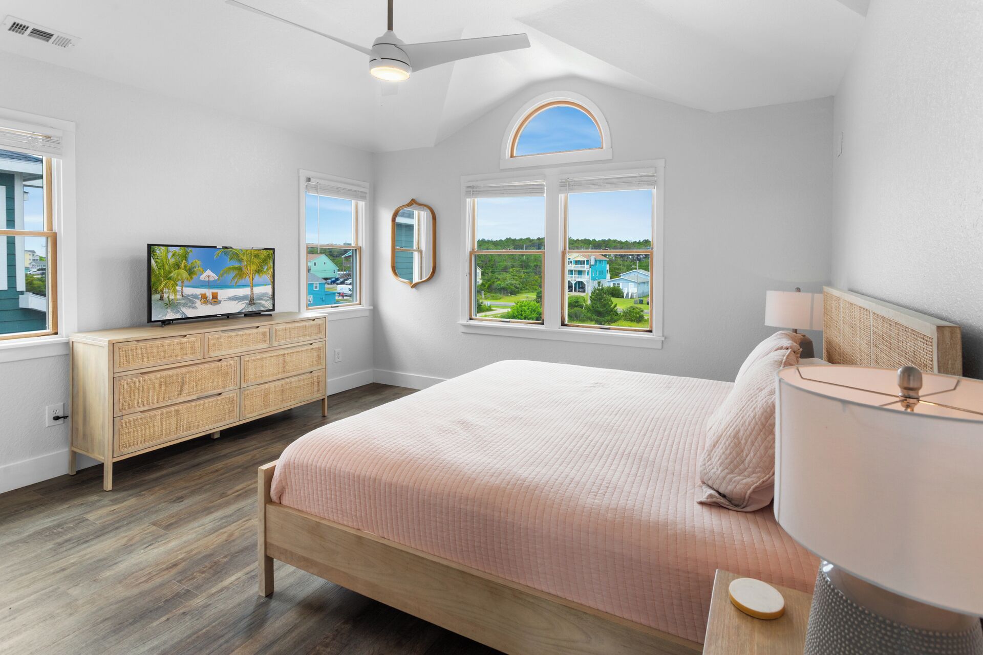 A bedroom with a bed, dresser, TV, and windows with a view.