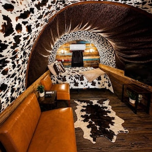 A cozy interior with a cowhide wall, a bed with a cowhide bedspread, a leather couch, and a cowhide rug.