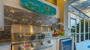 A stainless steel grill with a Bull logo, a decorative plate above it, and a bowl of fruit on the counter. - Canal Views, Gulf Access, Heated Saltwater Pool, Bikes - Coastal Serenity - Roelens (Cape Coral)