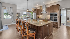 A spacious kitchen with a large island, wooden cabinets, and pendant lighting. - Canal Views, Gulf Access, Heated Saltwater Pool, Bikes - Coastal Serenity - Roelens (Cape Coral)
