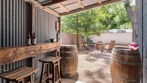 Un área de estar al aire libre de estilo rústico con mesas y sillas de madera, una barra de madera y barriles grandes.