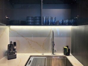 Una cocina moderna con un lavamanos de acero inoxidable, un bloque de cuchillos integrado y un estante de vidrio sobre el lavamanos.