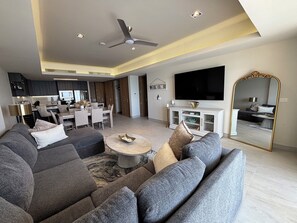 Una sala de estar moderna con un sofá modular, un comedor, una cocina y un televisor de pantalla plana grande.