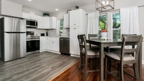 A modern kitchen with white cabinets, stainless steel appliances, and a dining area with a table and chairs. - Golden Cottage | 2/1.5, Washer/Dryer, Full Kitchen (Fredericksburg)
