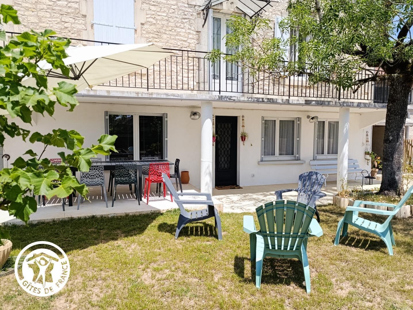 A two-story building with a balcony, outdoor seating area with chairs, and a grassy yard.