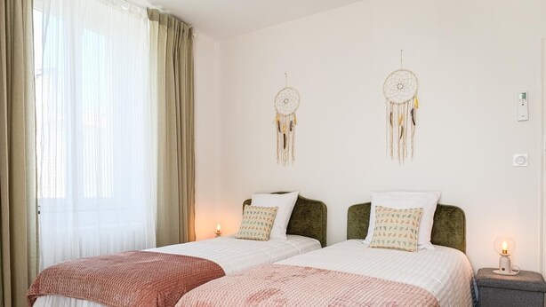 Ein Doppelbett mit zwei Kissen, ein Nachttisch mit Lampe und ein Traumfänger an der Wand.