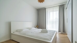 A modern bedroom with a large bed, a bedside table, and a window with curtains. - Park Śląski Charming Apartment (Katowice)