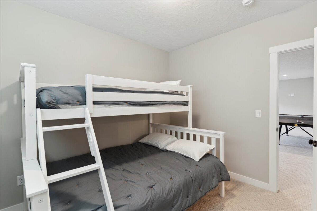 A bunk bed room with a desk and chair, a small table, and a door leading to another room.