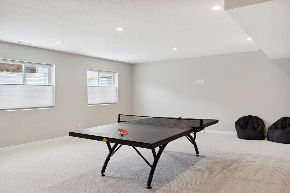 A room with a ping pong table, two windows with blinds, and two bean bags.