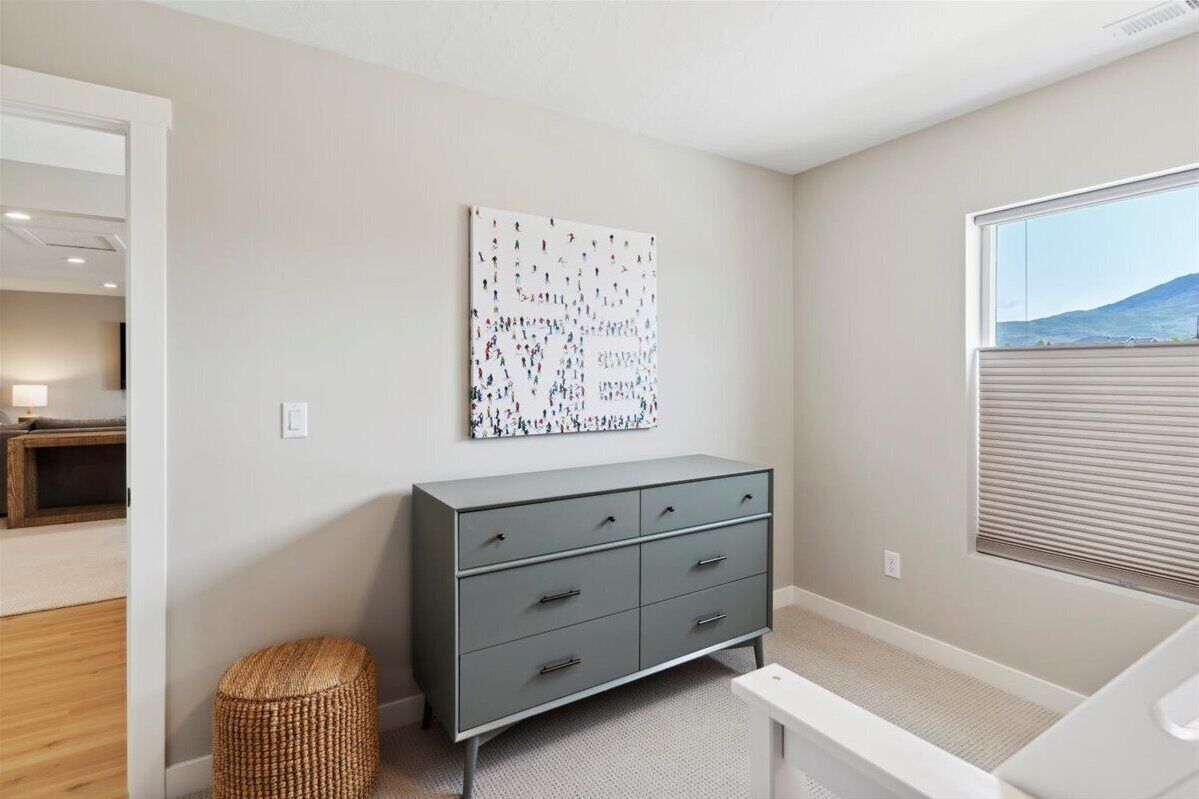 A room with a grey dresser, a woven stool, and a large abstract painting on the wall.