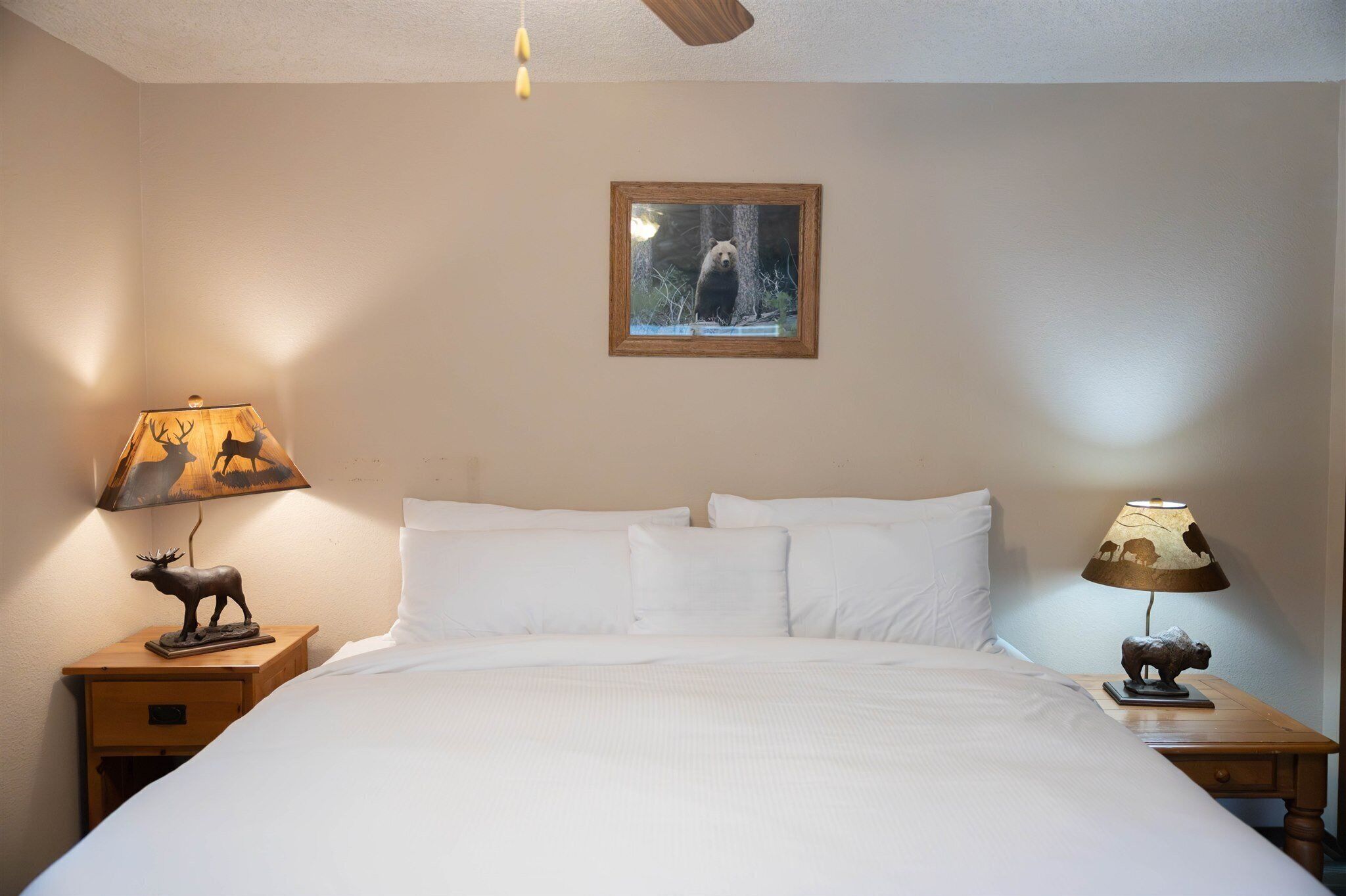 A neatly made bed with white linens, two bedside tables with lamps, and a framed picture of a bear on the wall.