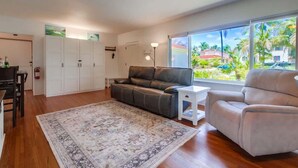 A living room with a sofa, armchair, and a large window with a view of palm trees.