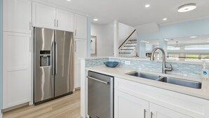 Una cocina moderna con gabinetes blancos, electrodomésticos de acero inoxidable, un salpicadero de azulejos azules y un lavamanos de acero inoxidable.