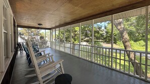 Une véranda couverte, dotée de bancs en bois et d’une balustrade, qui offre une vue sur un paysage verdoyant, avec des arbres et une route.