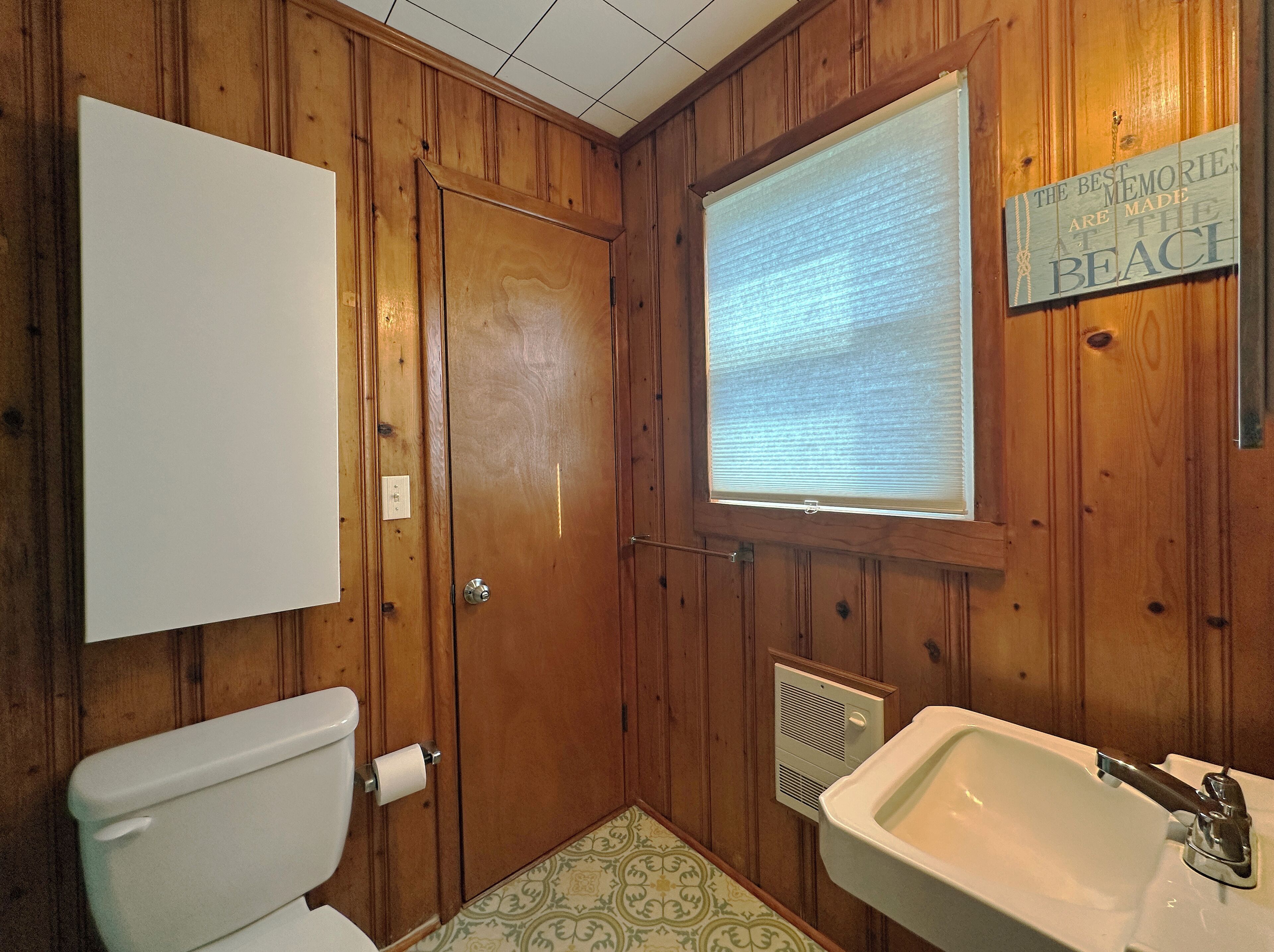 Un baño con paneles de madera, un inodoro, un lavabo y una ventana.
