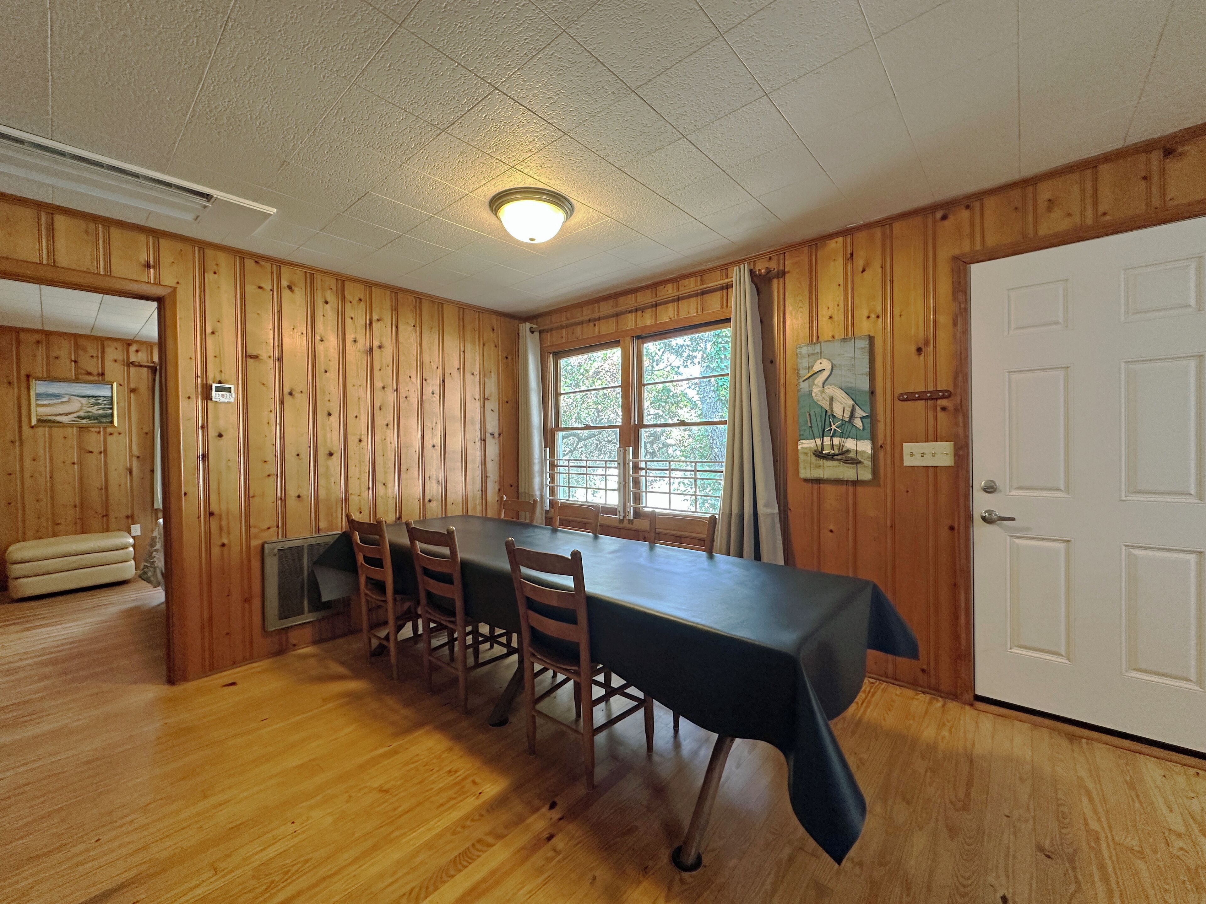 A dining area with a long table, wooden walls, and a door.