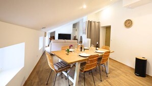 Ein Essbereich mit Holztisch, Korbstühlen und einem weißen Sofa im Hintergrund.