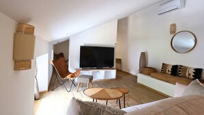 Ein modernes Wohnzimmer mit einem Flachbildfernseher, einem braunen Ledersessel, einem weißen Sofa und einem runden Couchtisch.