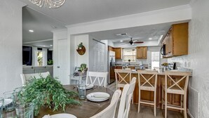 A modern kitchen with wooden cabinets, a dining area with a wooden table and chairs, and a bar area with stools. - Florida Breeze |Pool & Jacuzzi| 2-min walk to BCH (St. Augustine)