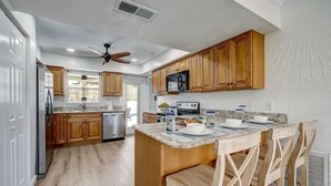 A modern kitchen with wooden cabinets, a granite countertop, and a central island with bar stools. - Florida Breeze |Pool & Jacuzzi| 2-min walk to BCH (St. Augustine)