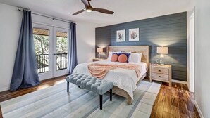 A bedroom with a bed, a bench, a nightstand, a ceiling fan, and a view through a sliding door. - Florida Breeze |Pool & Jacuzzi| 2-min walk to BCH (St. Augustine)