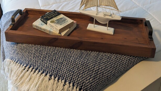 A neatly made bed with a sailboat model, a tray with books, and a houndstooth throw on a bed with a white headboard and dark pillows. - Marina Across the Street! Park your boat & Trailor here! (Ludington)