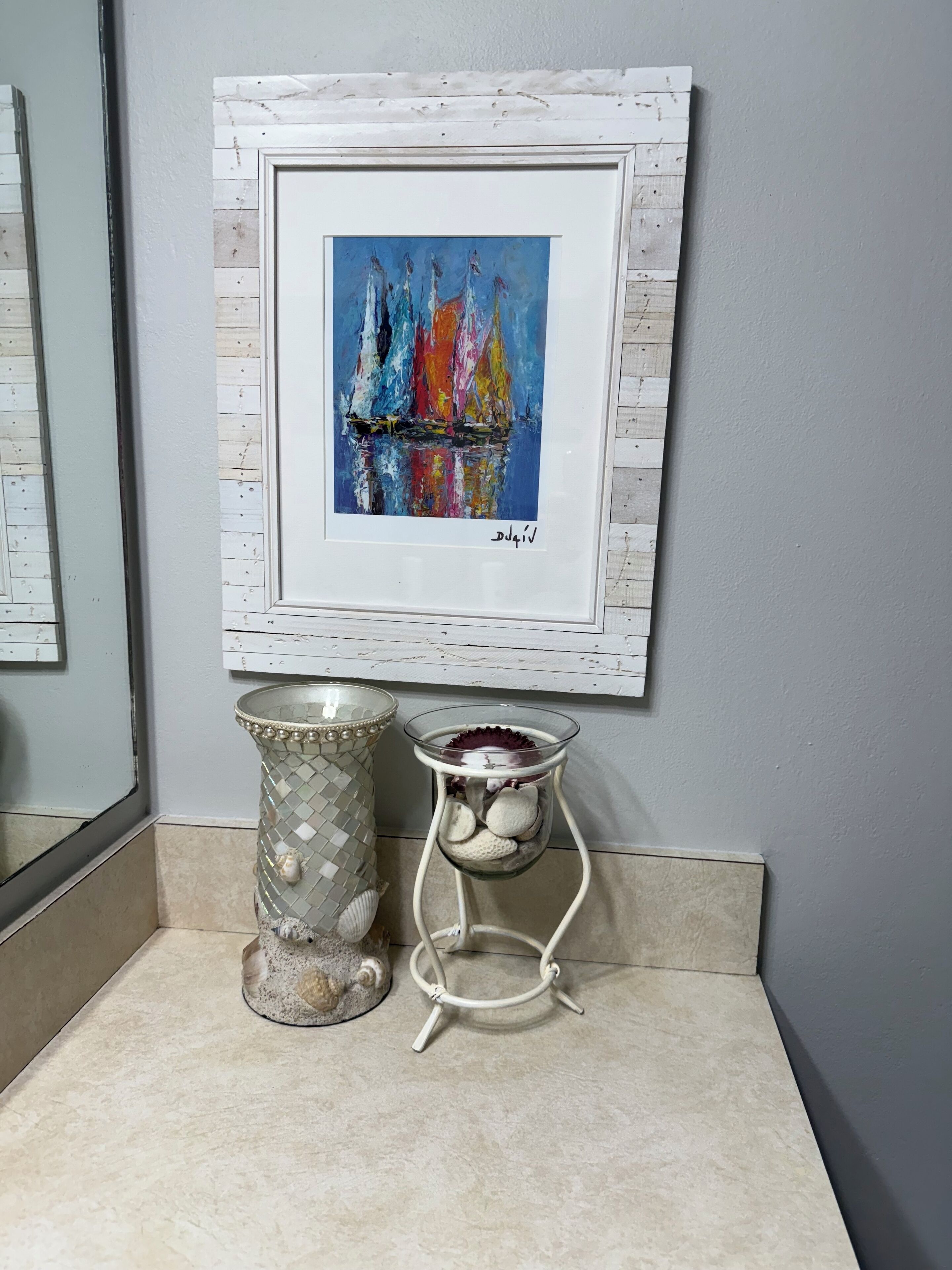 A framed painting of sailboats on a wall, a decorative glass vase, and a metal candle holder.