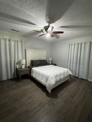 Une chambre à coucher avec un lit, des tables de chevet, un ventilateur de plafond et des rideaux.