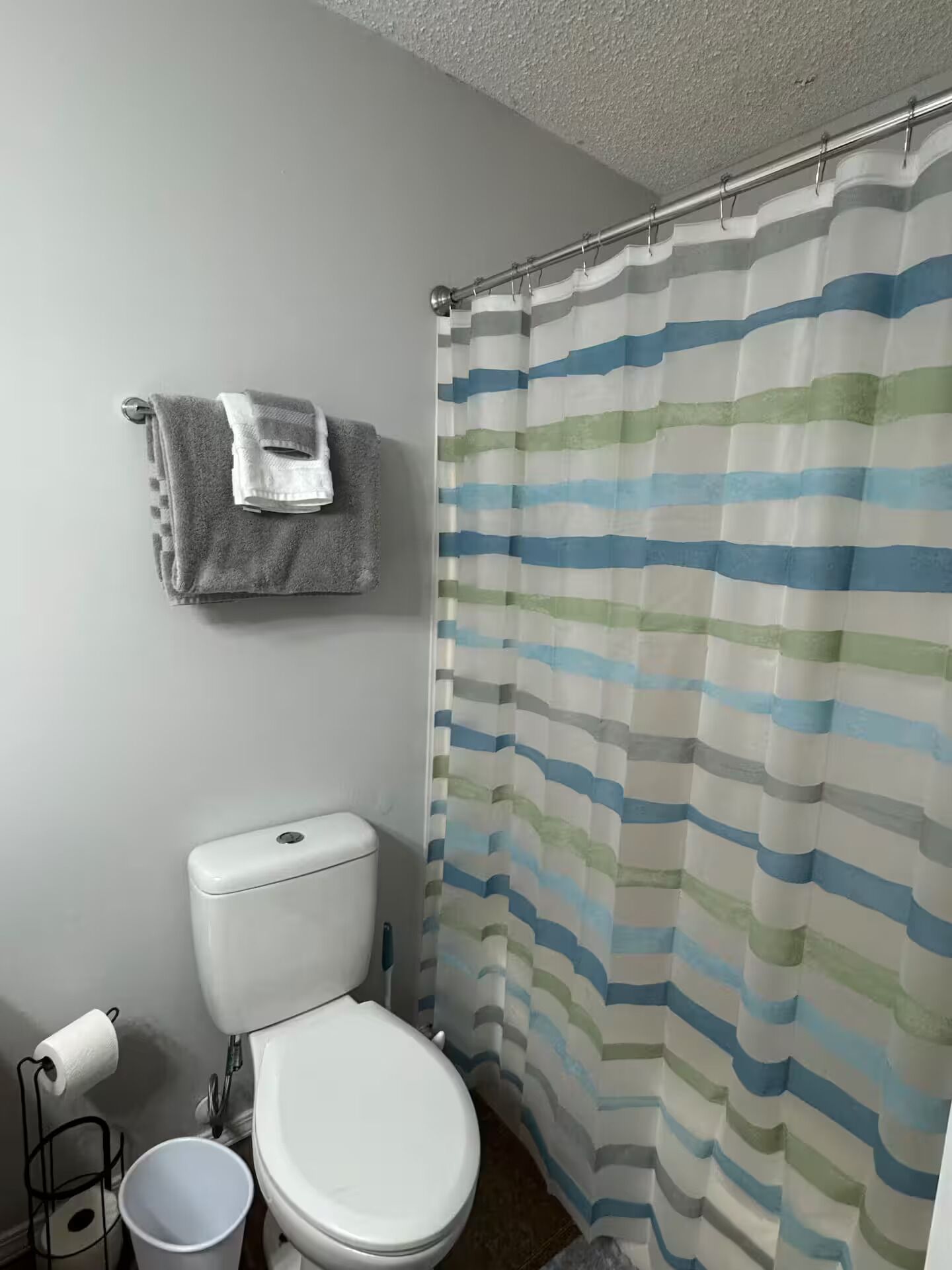 A bathroom with a striped shower curtain, a toilet, a sink, and a towel rack with a towel.