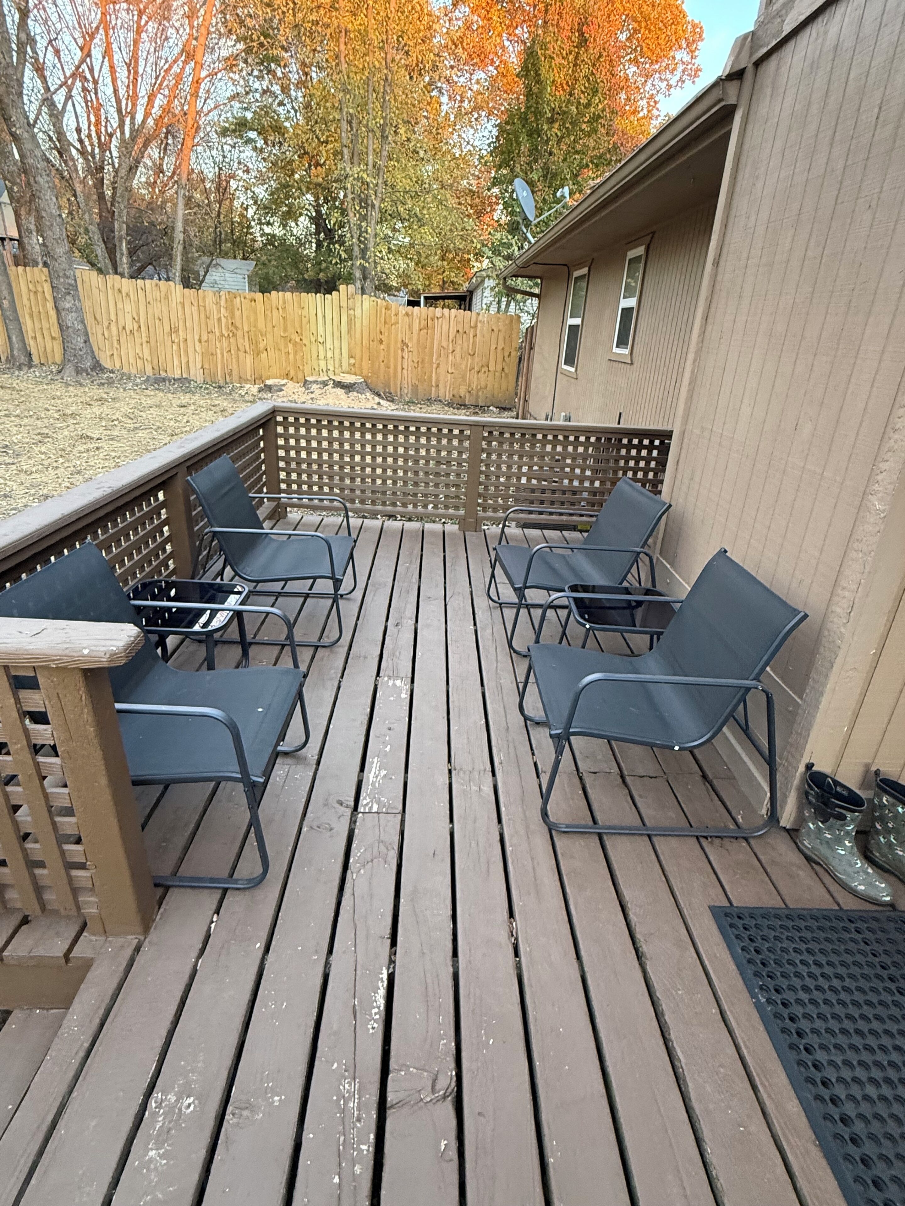 A wooden deck with six black chairs, a small table, and a wooden fence.