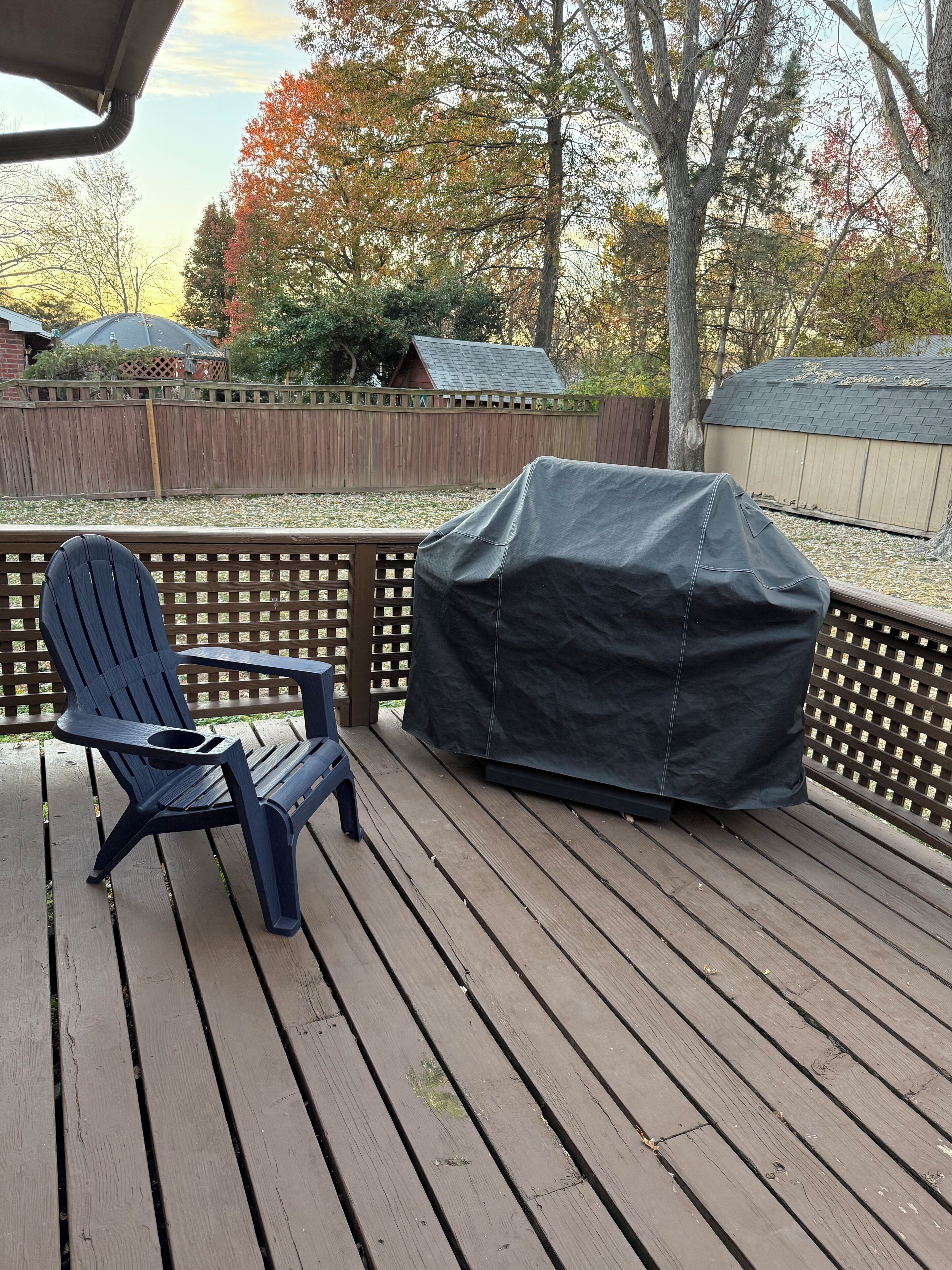 A wooden deck with a covered grill and a single Adirondack chair.