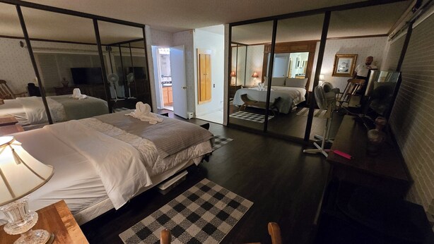 Een hotelkamer met een groot bed, een bureau met lamp, een stoel, een klein tafeltje met een vaas en een geruit tapijt.