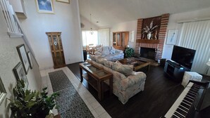 Een woonkamer met een bank, salontafel, open haard, televisie en een piano.