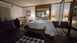 A neatly arranged bedroom with a large bed, a wooden chair, a dresser, and a mirror.